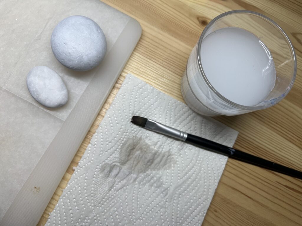 Maalatut kivet, vesilasi ja sivellin